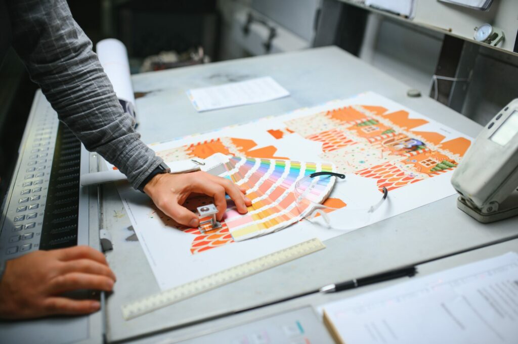 Print house worker controlling printing process quality and checking colors with magnifying glass